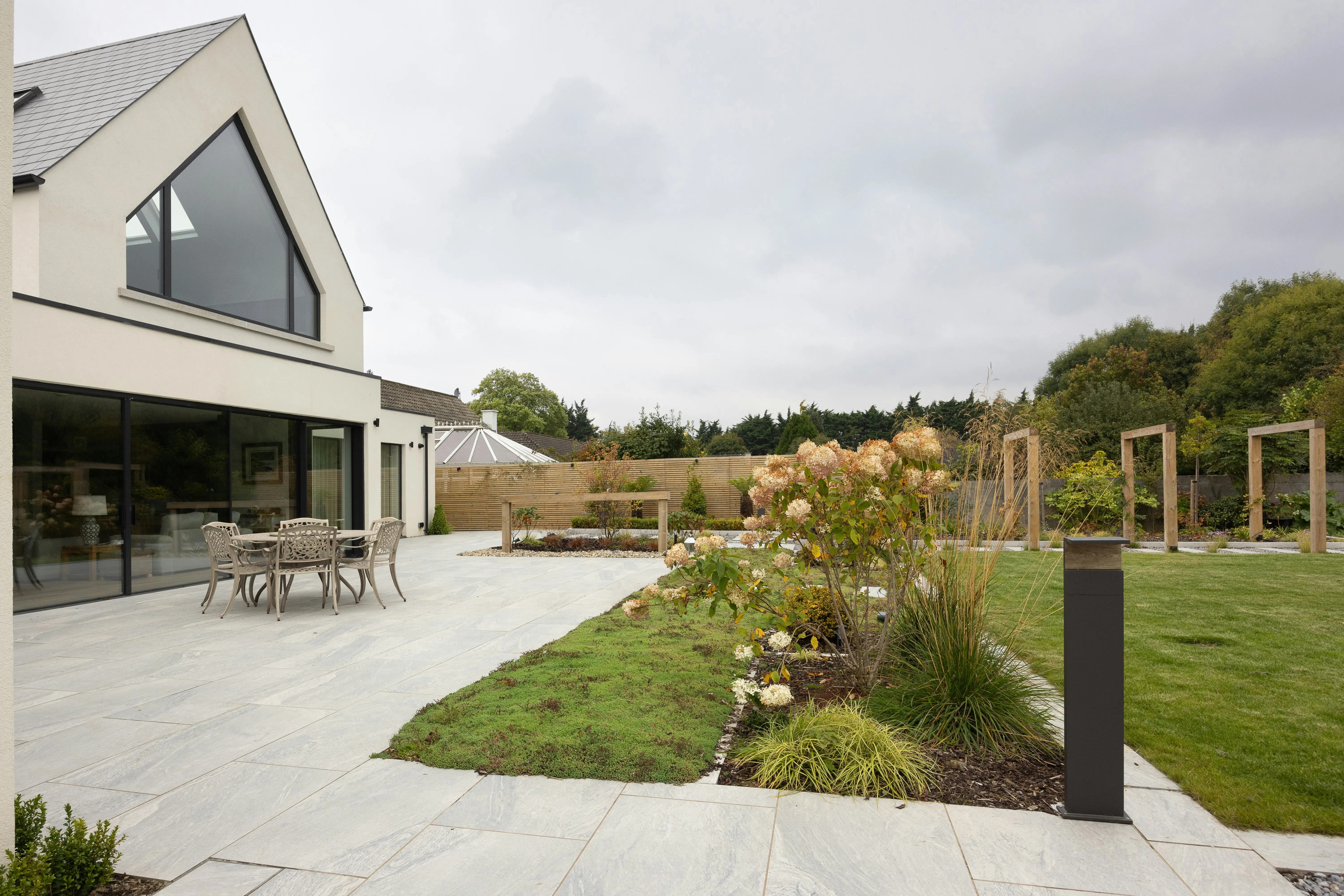 Large light grey modern patio slabs extending from a house to a landscaped garden area.