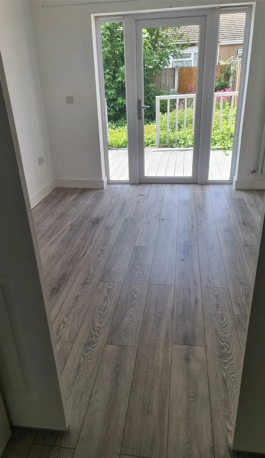 An empty, clean room with laminate flooring and patio doors leading to a garden, illustrating a professionally cleared property.