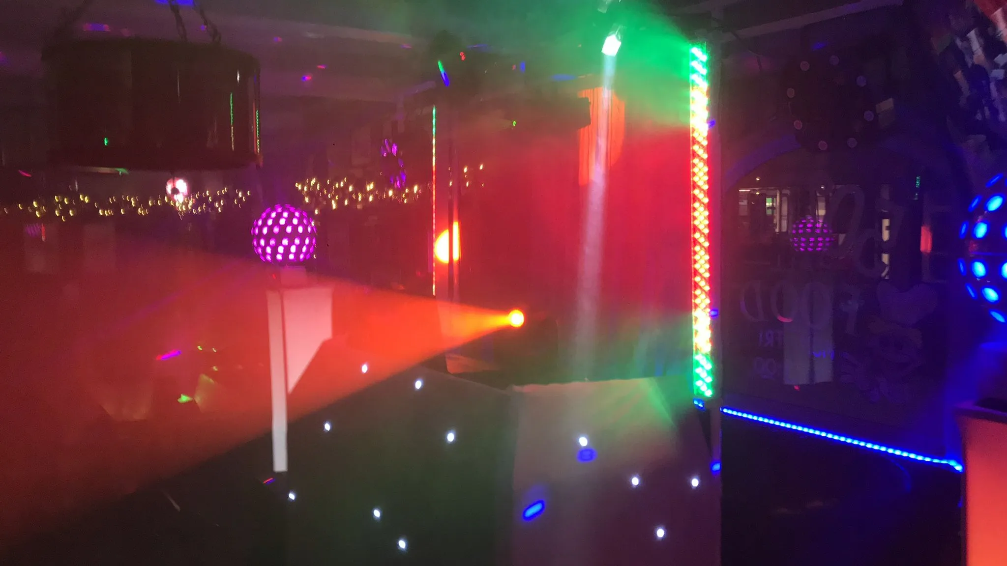 Vibrant DJ setup with colourful disco lights, a purple disco ball, and LED effects for an event.