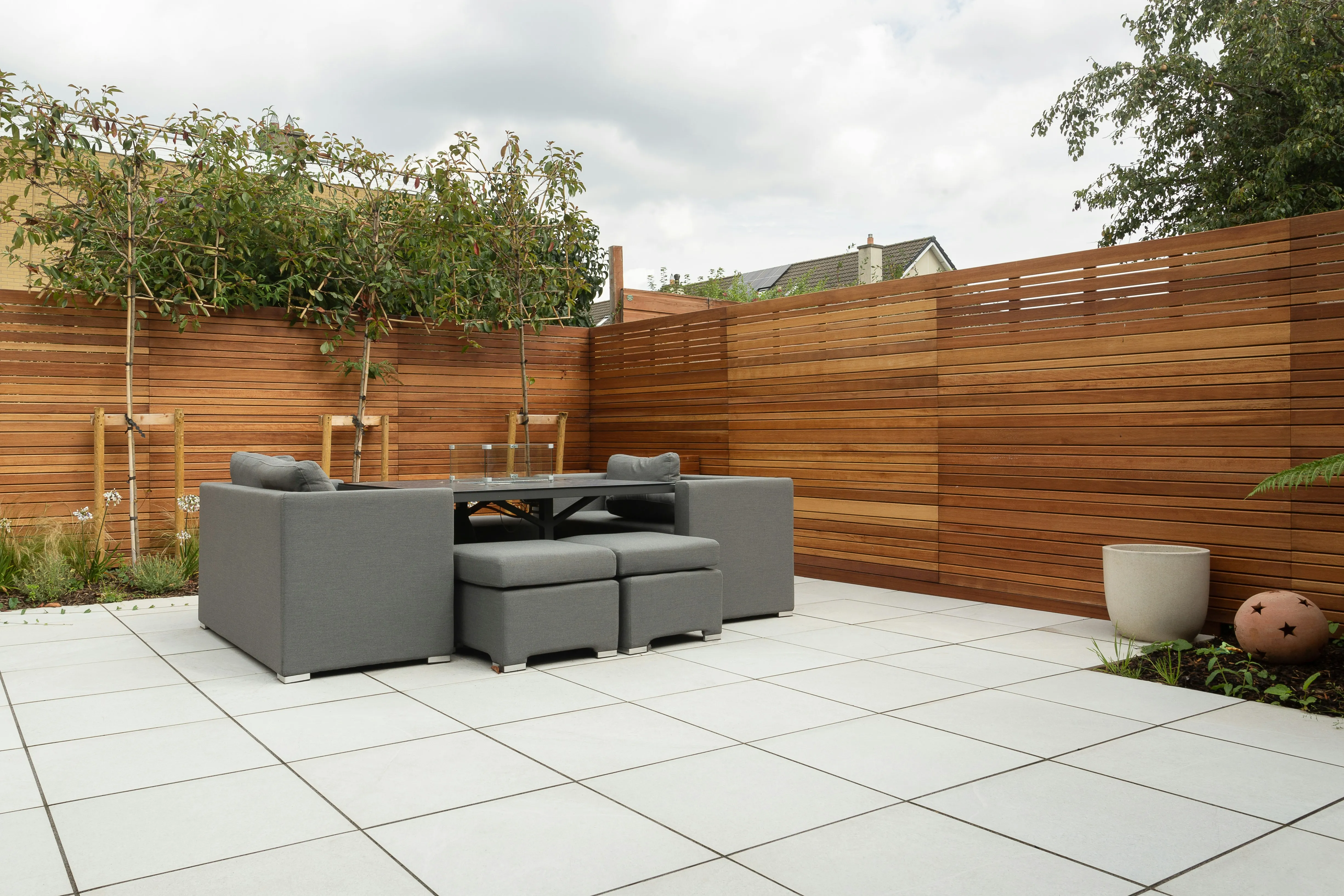 Modern garden patio with large light grey paving slabs and slatted wooden fence