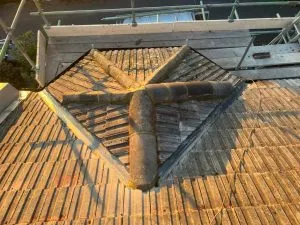 Close-up of a newly installed or repaired tiled roof junction, highlighting the precise placement of roof tiles and ridge capping at an angle on a pitched roof.