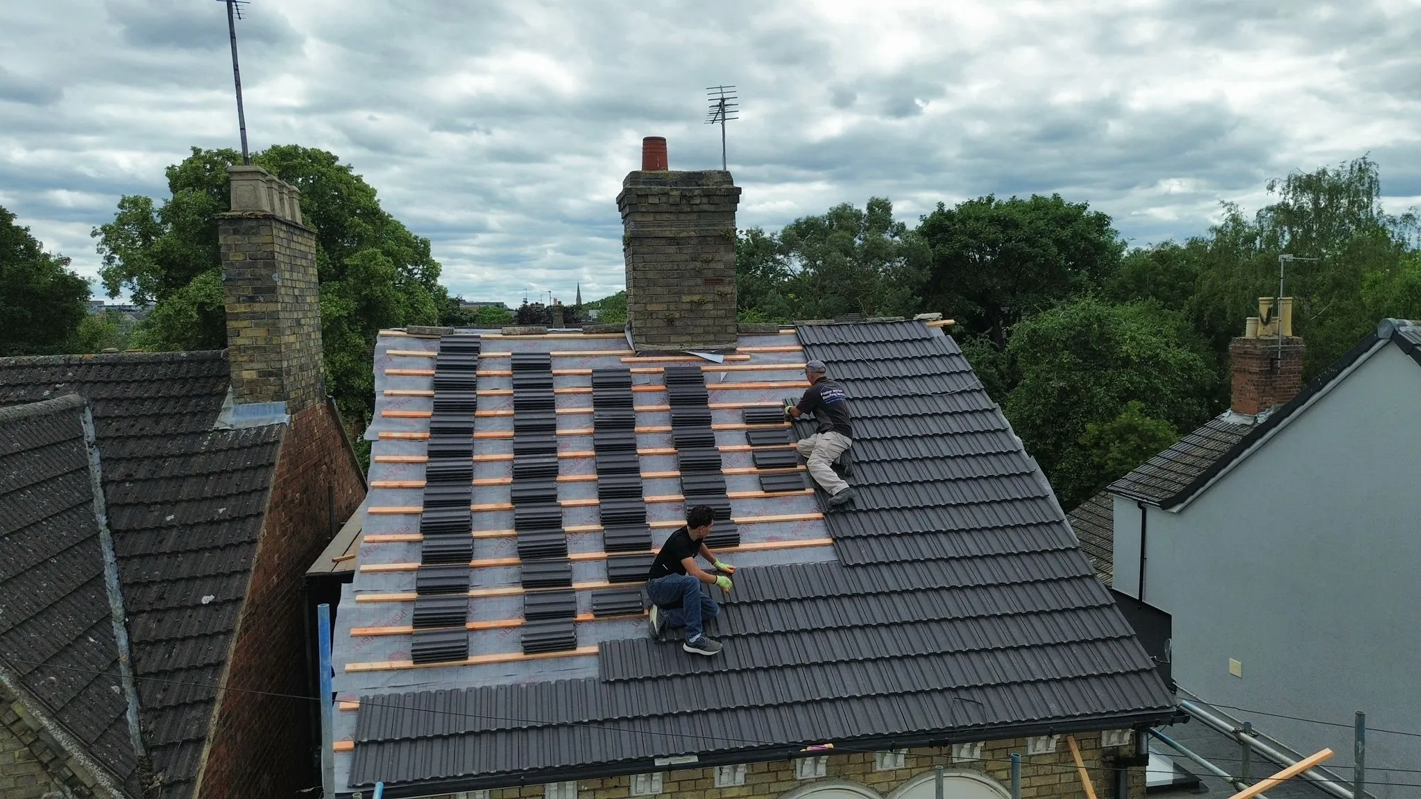 Two roofers installing new dark grey concrete tiles on a pitched roof in Spalding, Lincolnshire.