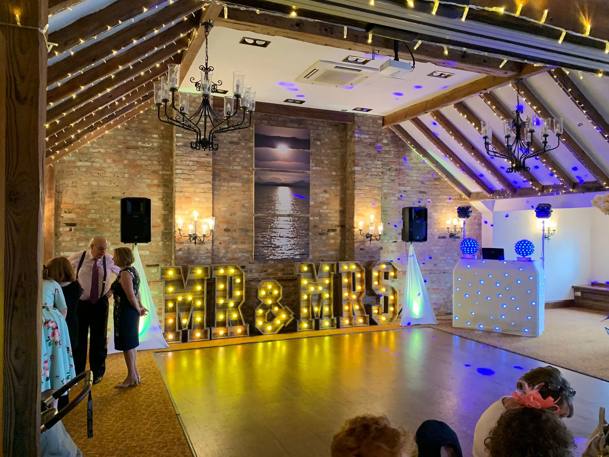 Elegant wedding reception setup in a rustic barn venue with a custom DJ booth and warm uplighting