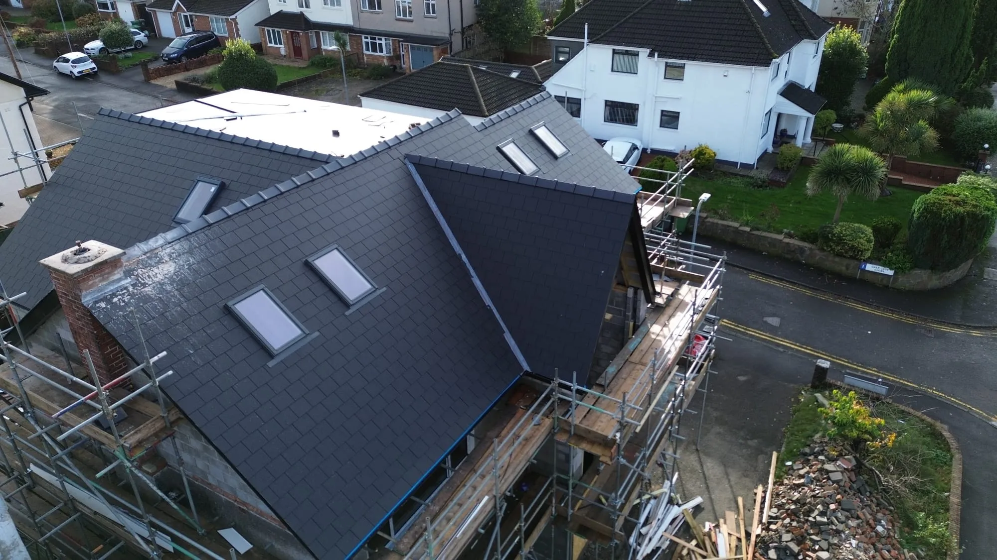 Aerial view of a new dark grey tiled roof with Velux windows being installed on a residential property, surrounded by scaffolding.