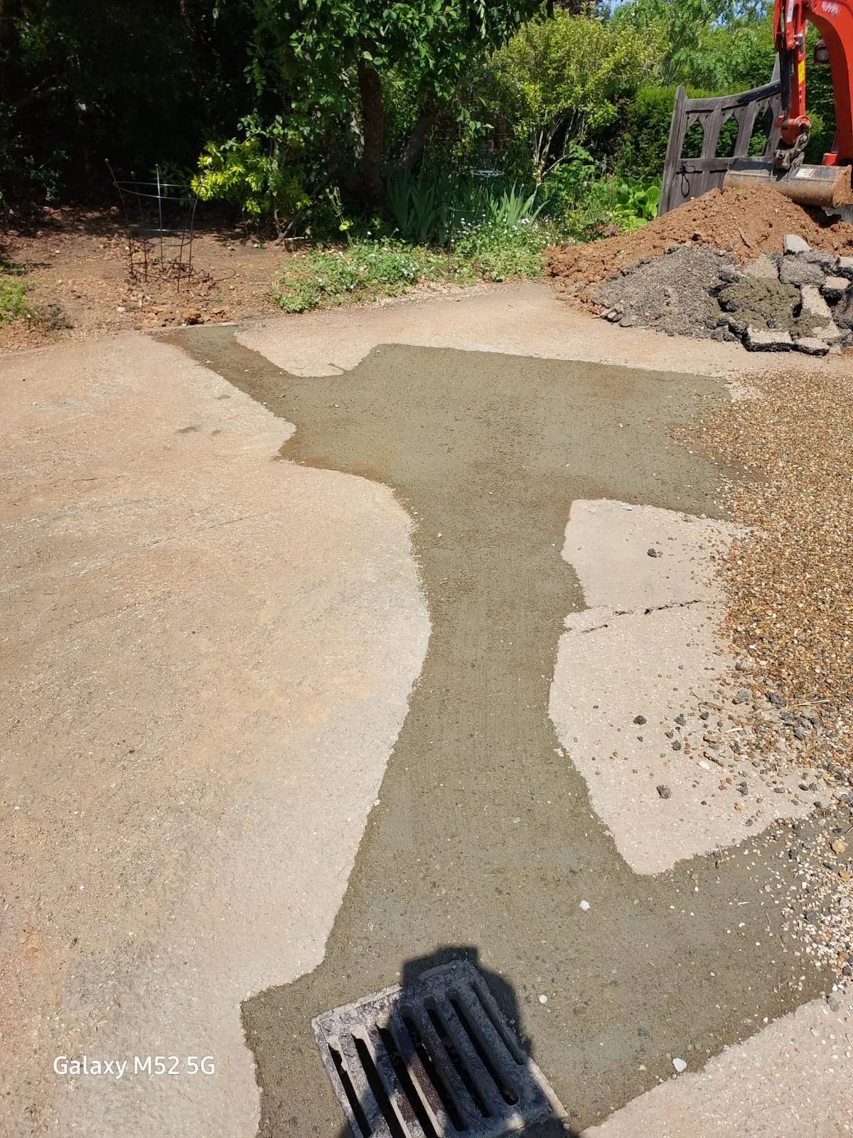 An outdoor drain showing recent concrete work for a drain repair or new installation, with excavation debris and an excavator nearby.