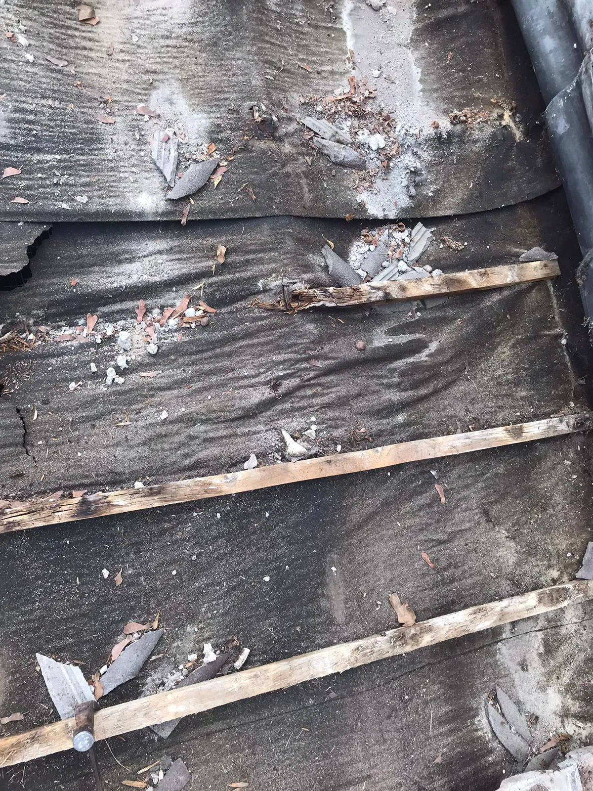 Damaged roof surface with visible old felt, wooden battens, and scattered debris, illustrating the need for roof repair services.