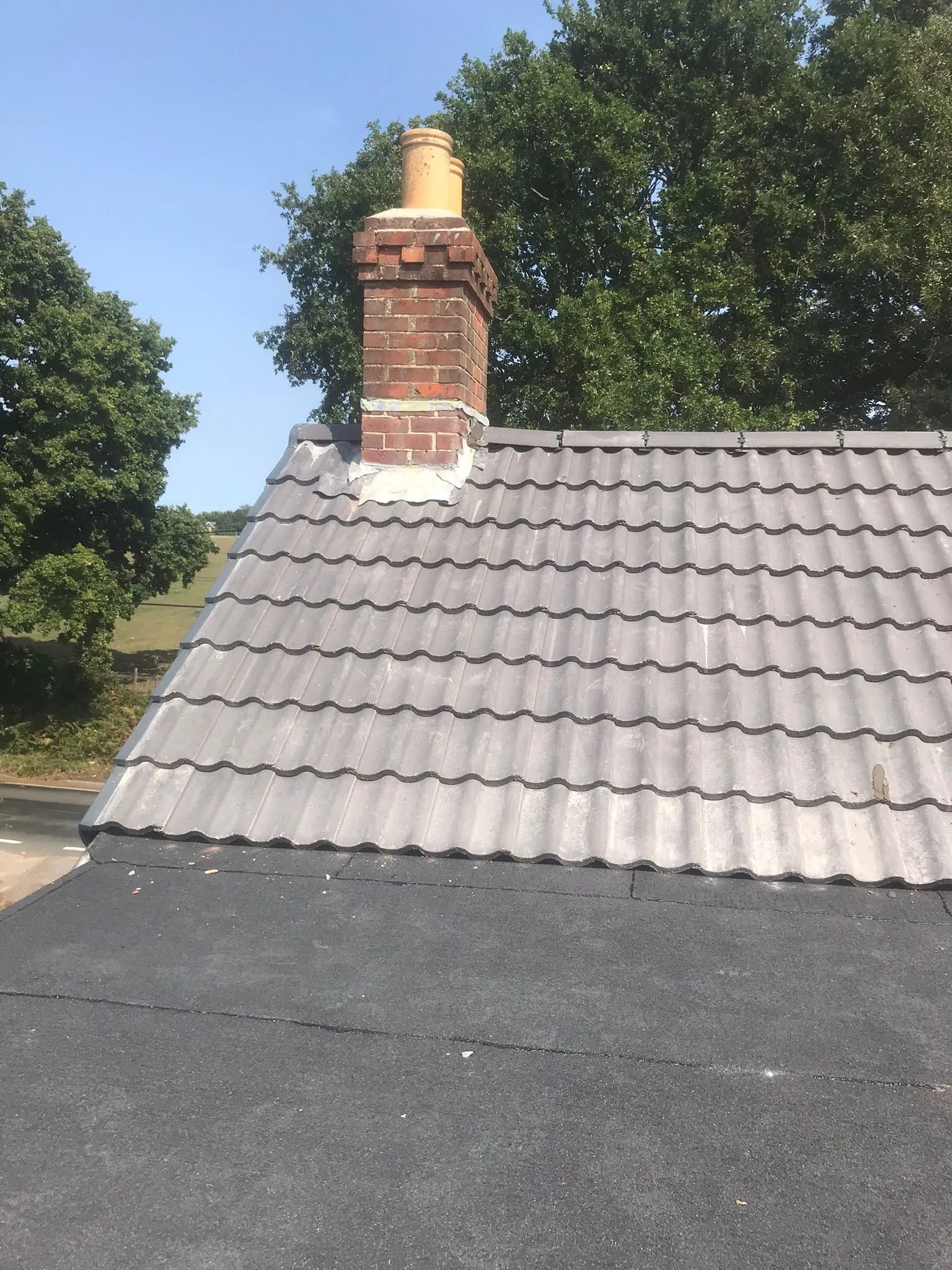Well-maintained tiled and flat roof with a brick chimney on a sunny day, showcasing different roofing materials.