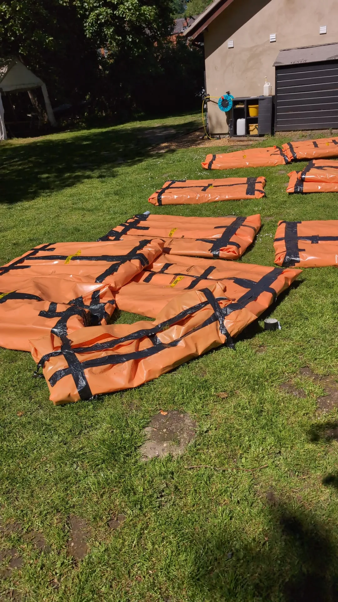 Asbestos waste packaged in bright orange hazardous waste bags, sealed with black tape and warning labels, awaiting collection on a green lawn.