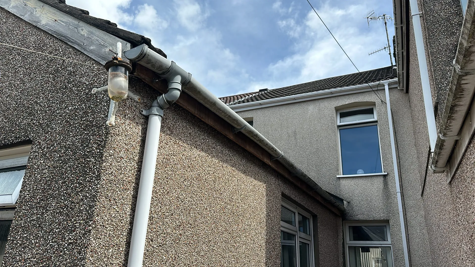 Dirty uPVC gutter and downpipe on a house exterior, showing accumulated debris.