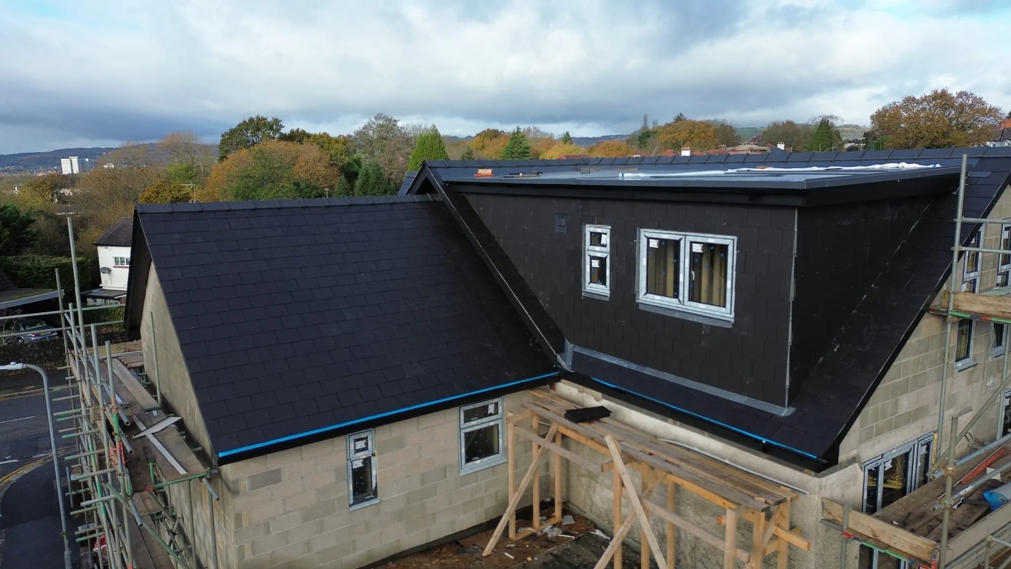 Newly installed dark tiled pitched roof and a flat roof on a modern residential property under construction.