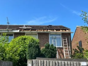 A house undergoing roof replacement, with the old tiles removed and the wooden roof structure visible.