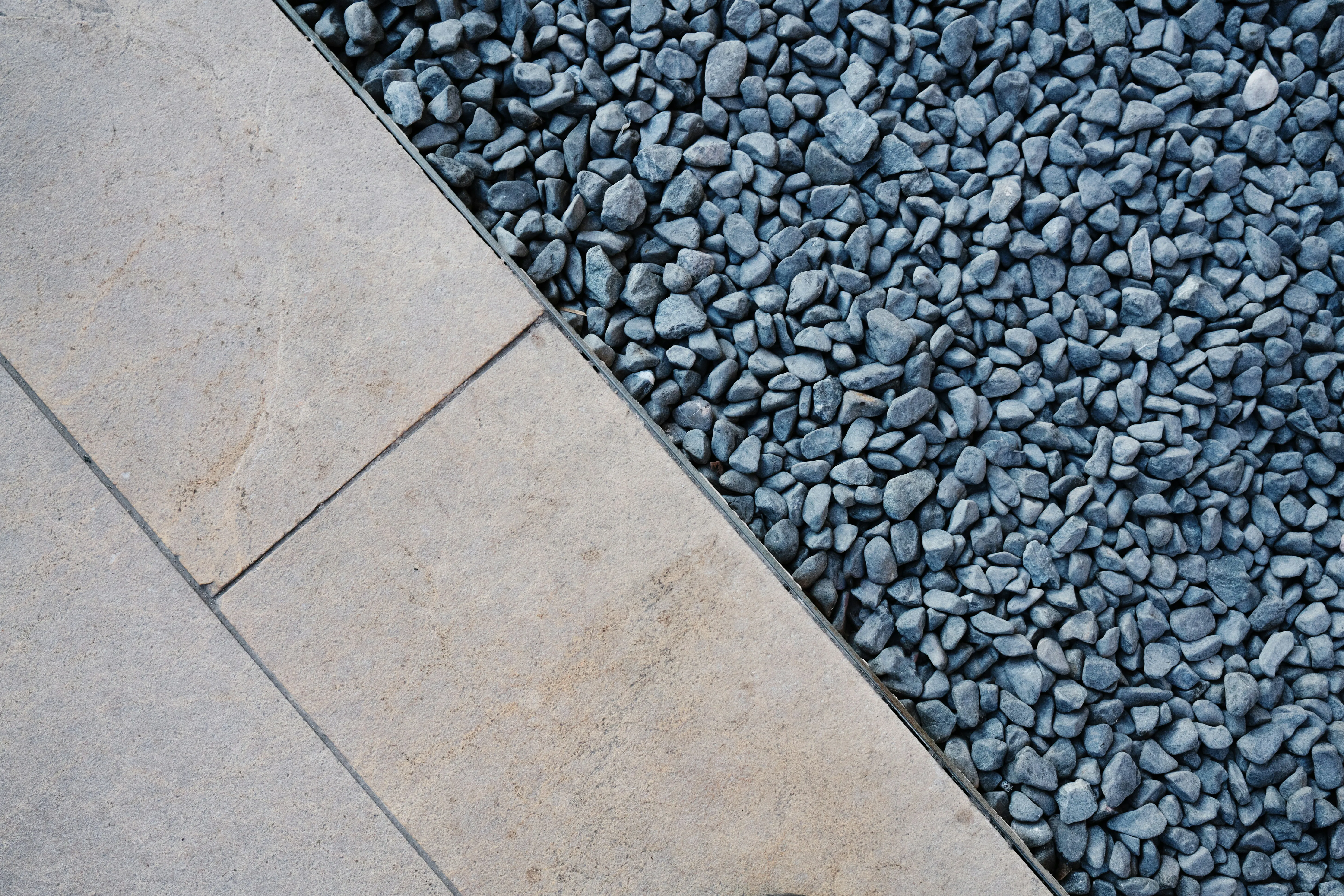 Close up texture of light paving slabs meeting dark grey gravel.
