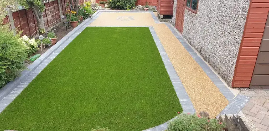 Modern garden with artificial lawn, light coloured resin bound patio and path, and grey block border.