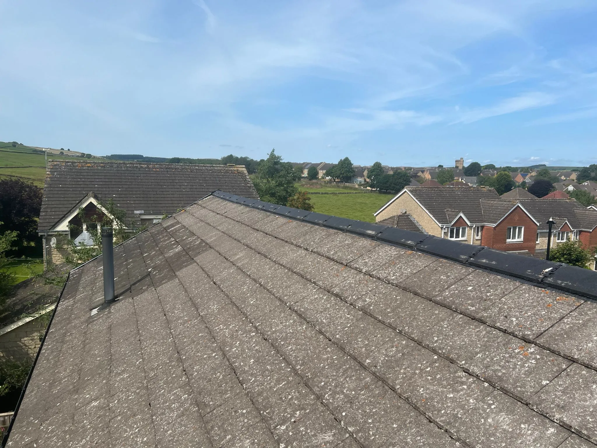 A pitched roof with weathered grey tiles overlooking houses and fields in South Yorkshire