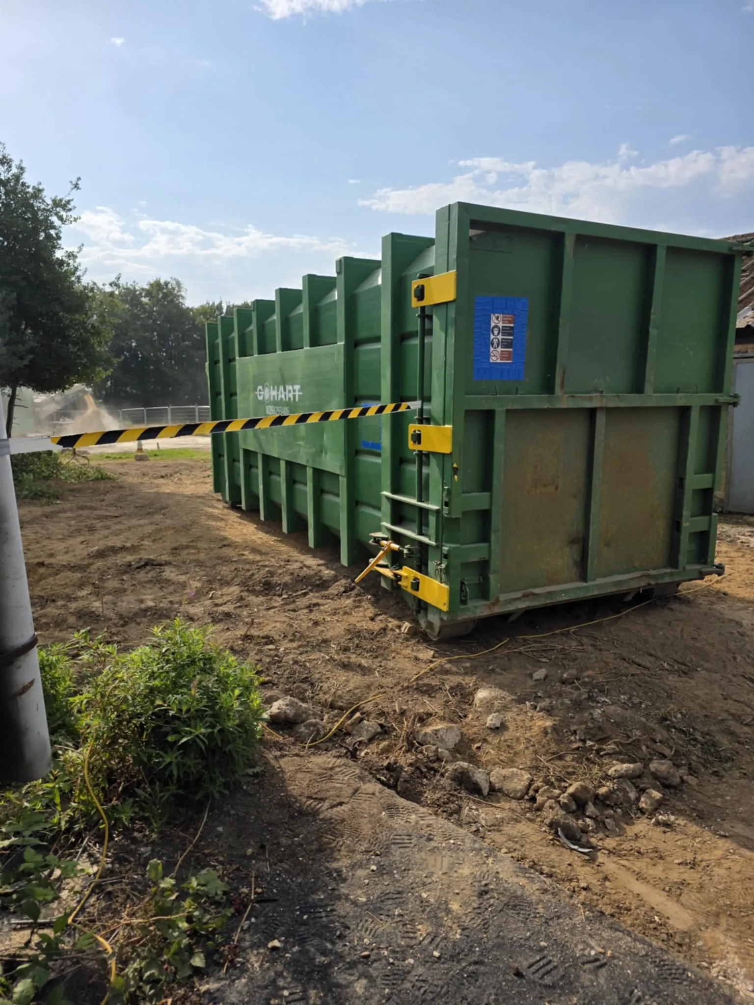 Green industrial waste skip with black and yellow warning tape on a construction or asbestos removal site