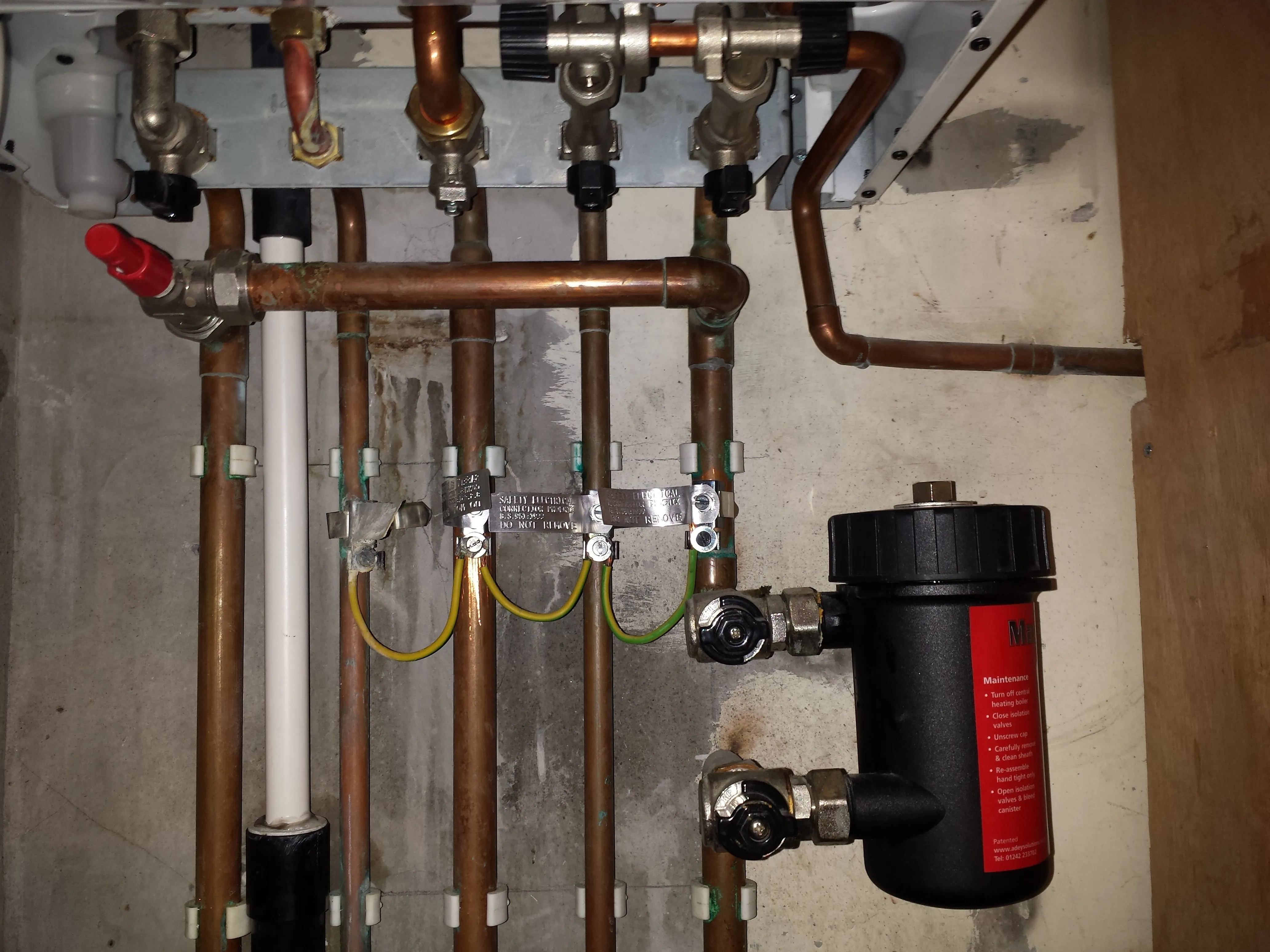 Detailed view of boiler connections, including copper pipes, a black magnetic filter, and earthing clamps.