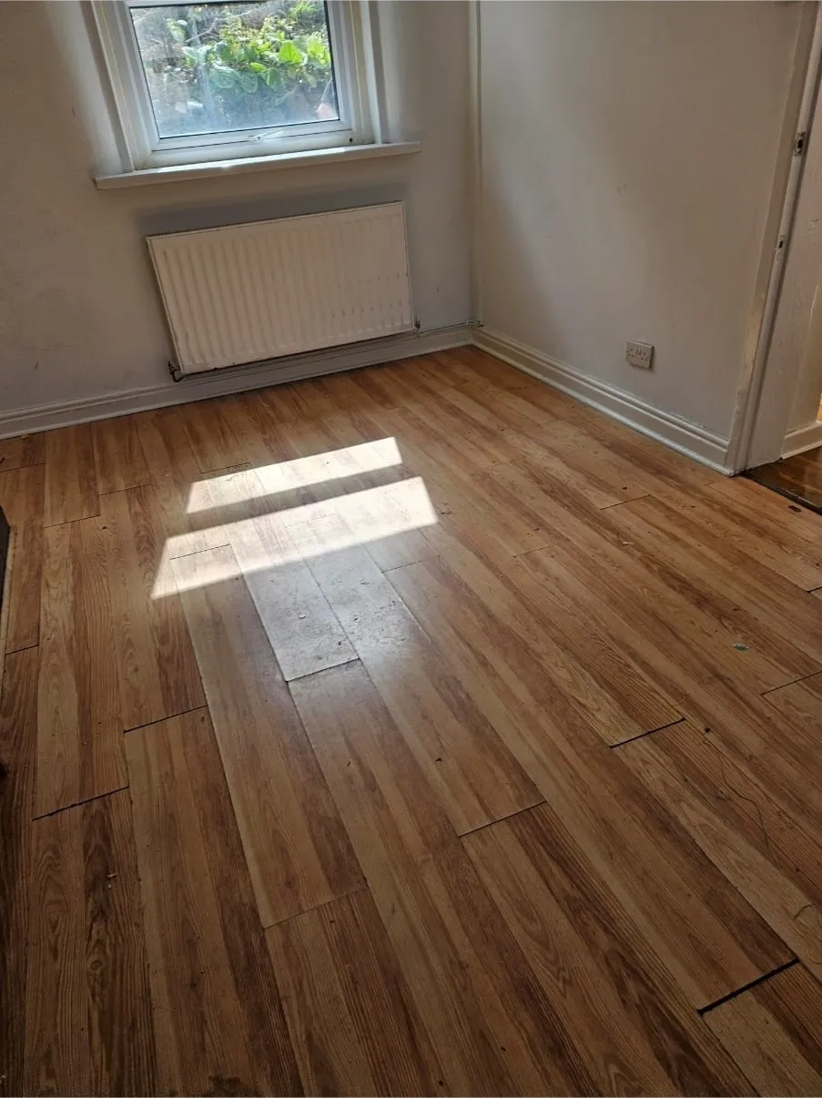 Empty room with wooden laminate flooring and a window after a professional house clearance service.