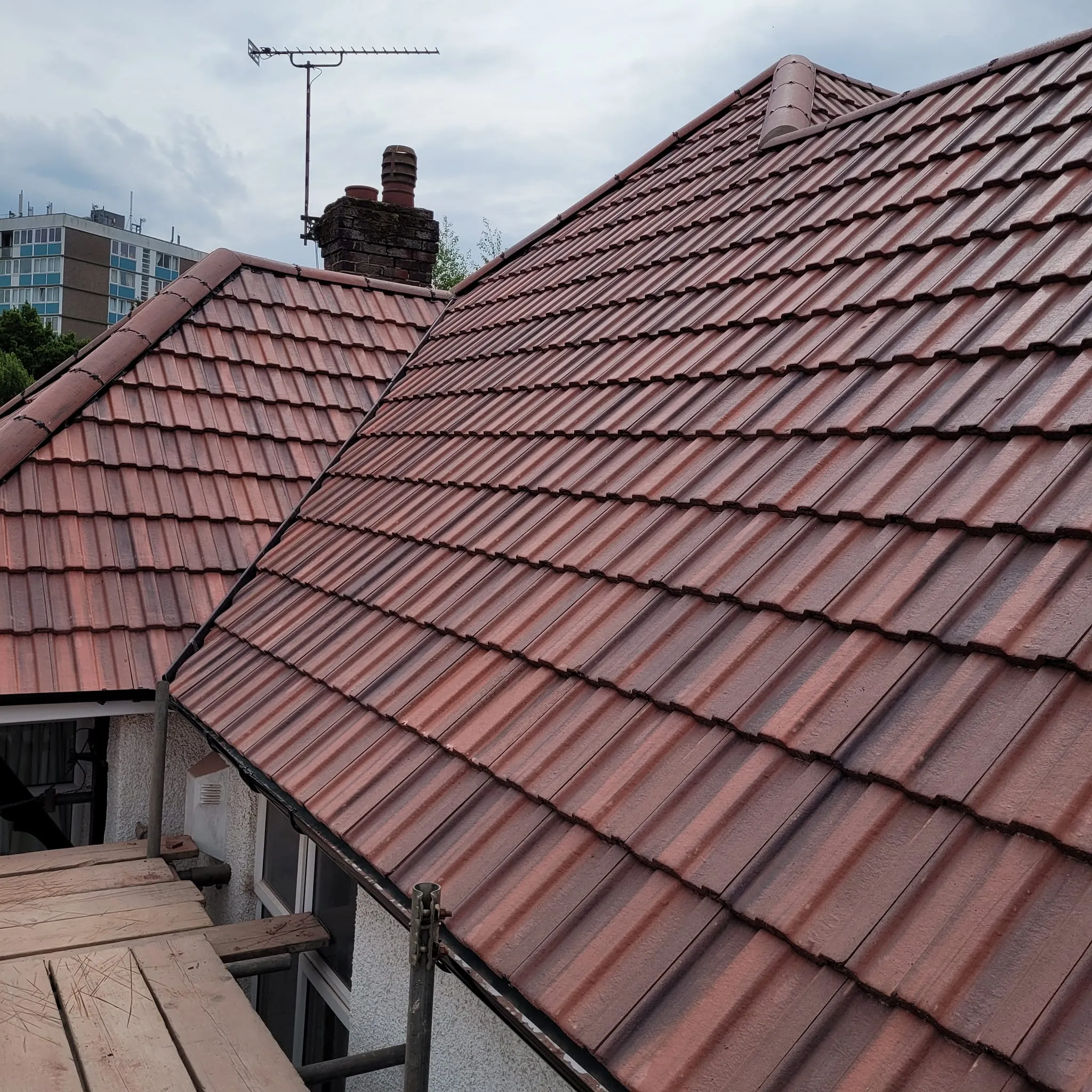 Newly installed pitched roof with tiled finish, chimney, and scaffolding