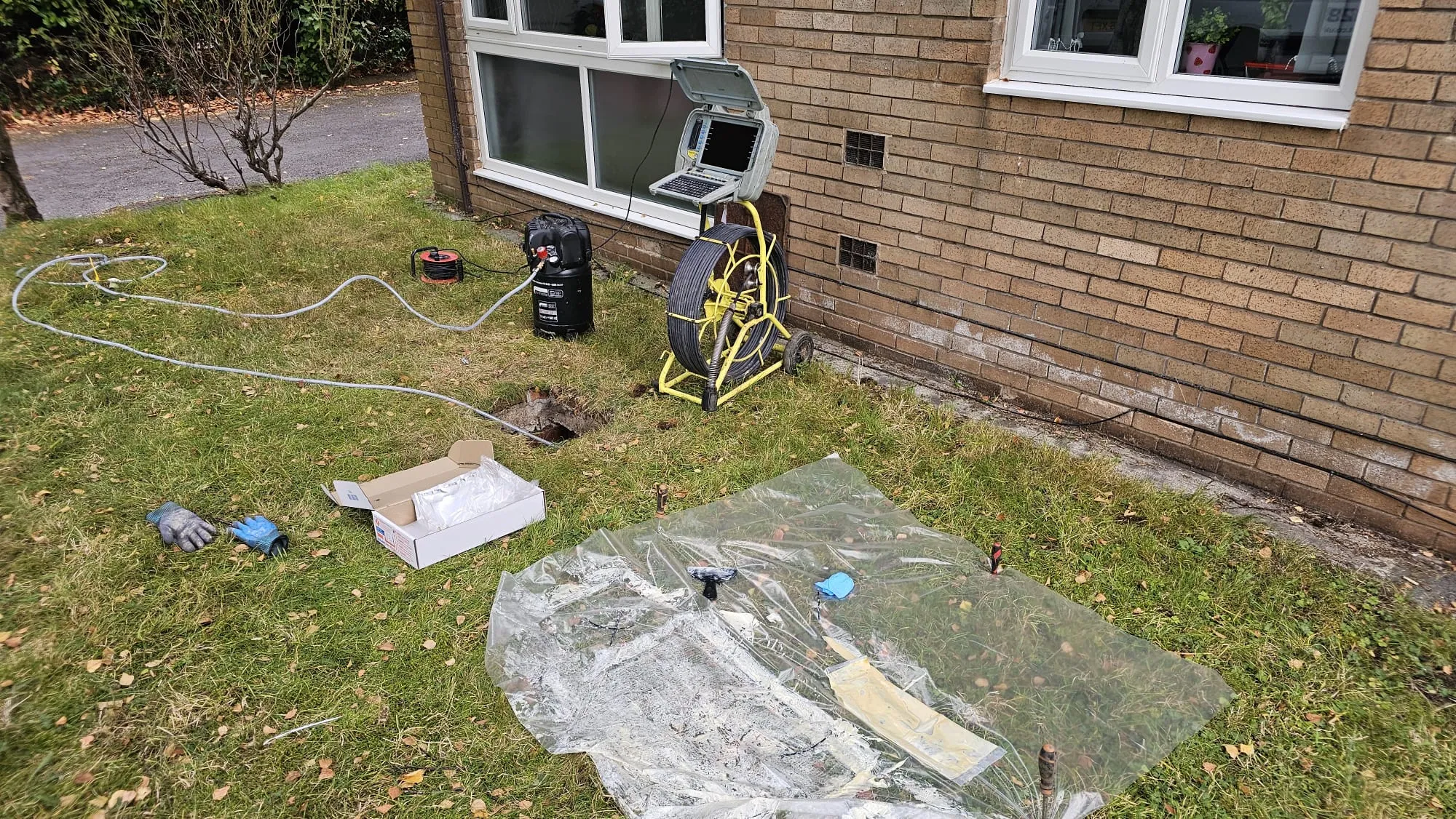 CCTV drain survey equipment with a camera reel and monitor on a lawn next to a house