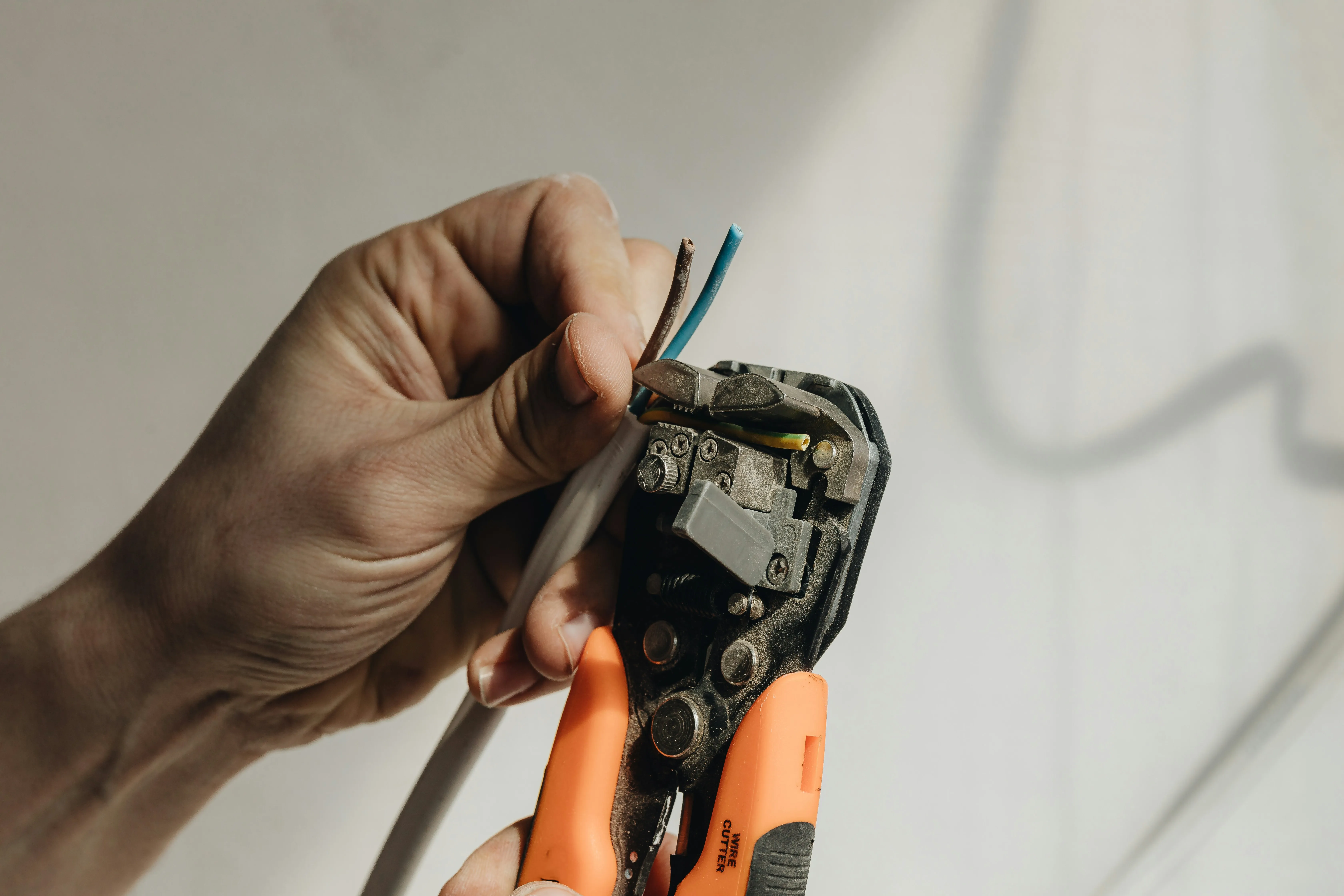 Electrician stripping the insulation from electrical wires with a professional wire stripping tool.