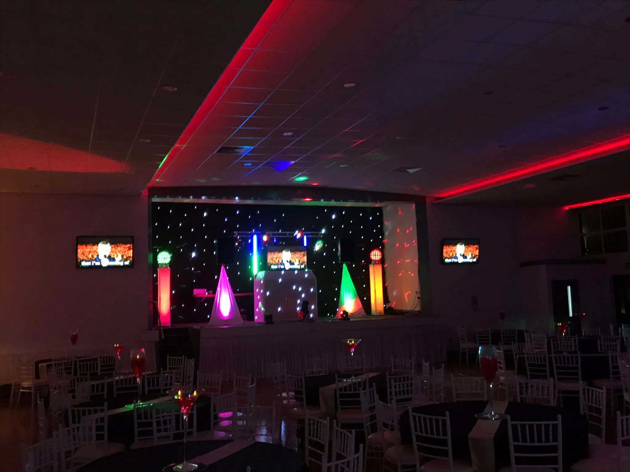 A colourful event venue setup with a DJ stage, large screens, and vibrant LED lighting.
