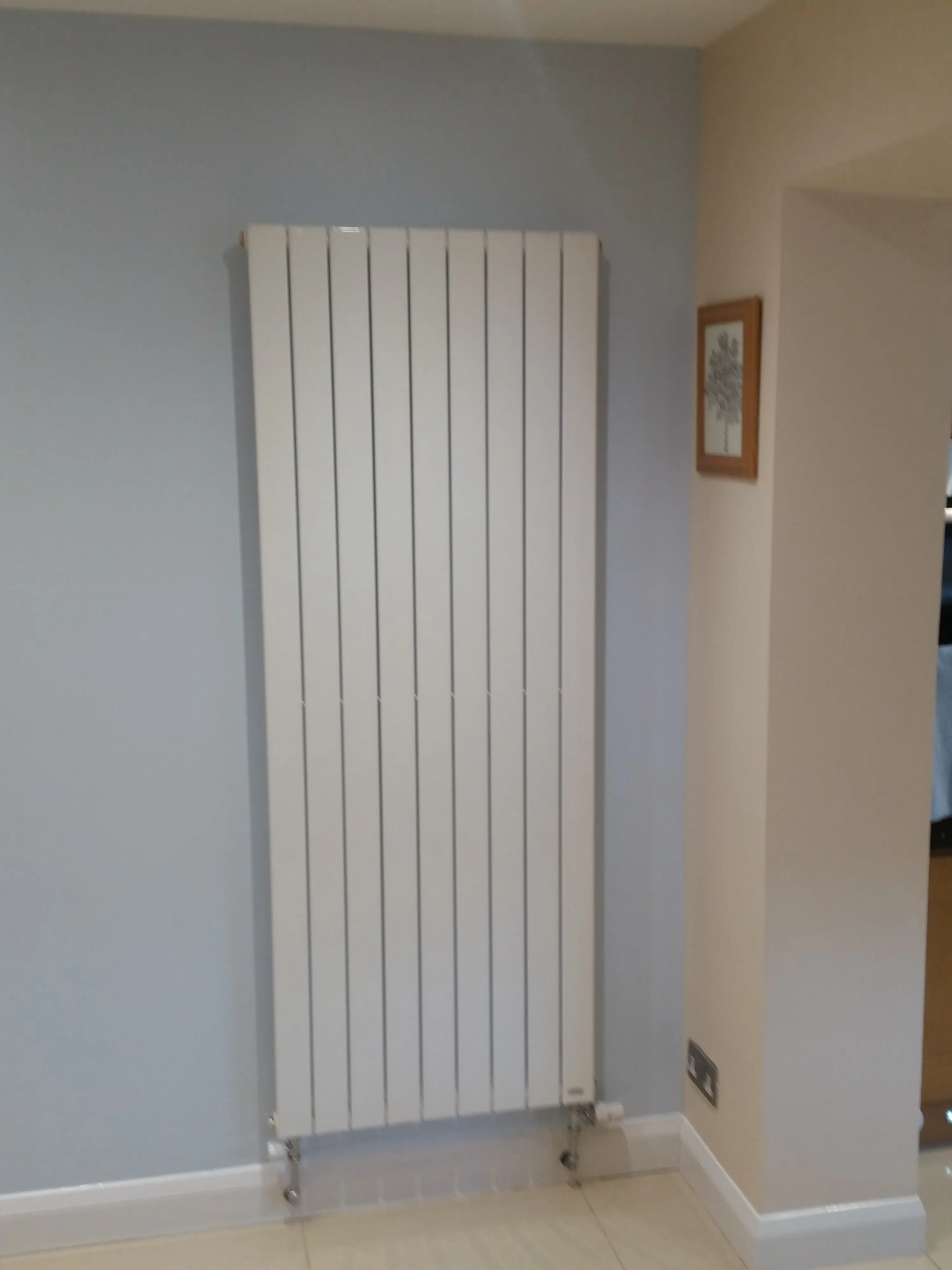 A modern vertical radiator installed on a blue wall