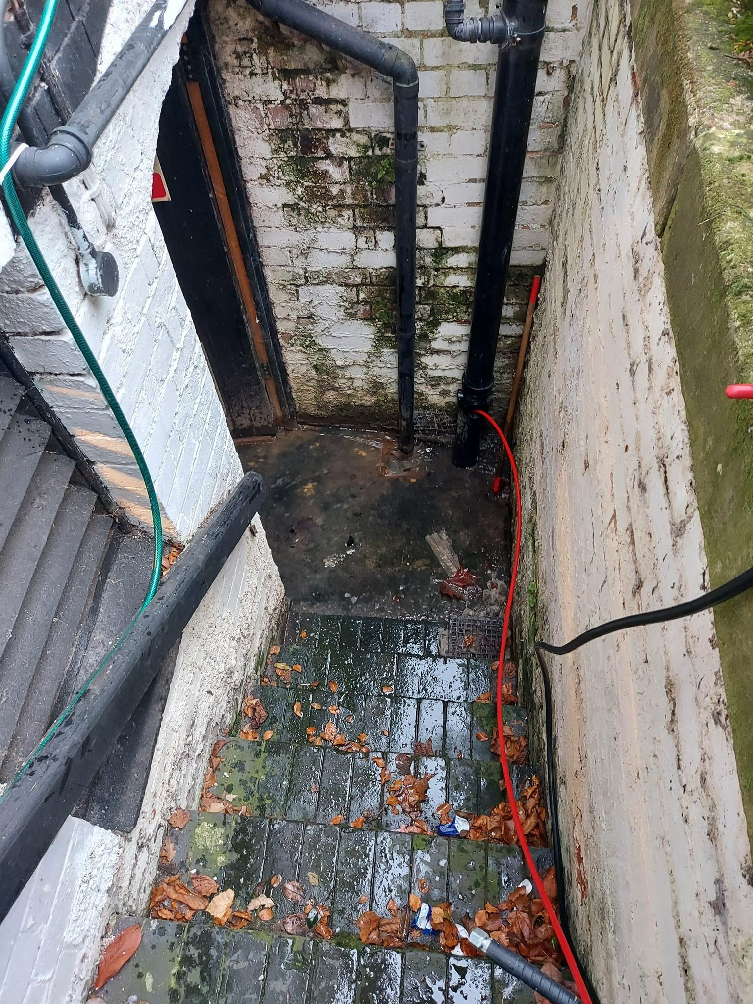 Standing water in a property's sunken area due to a blocked drain, with pipes and steps visible.
