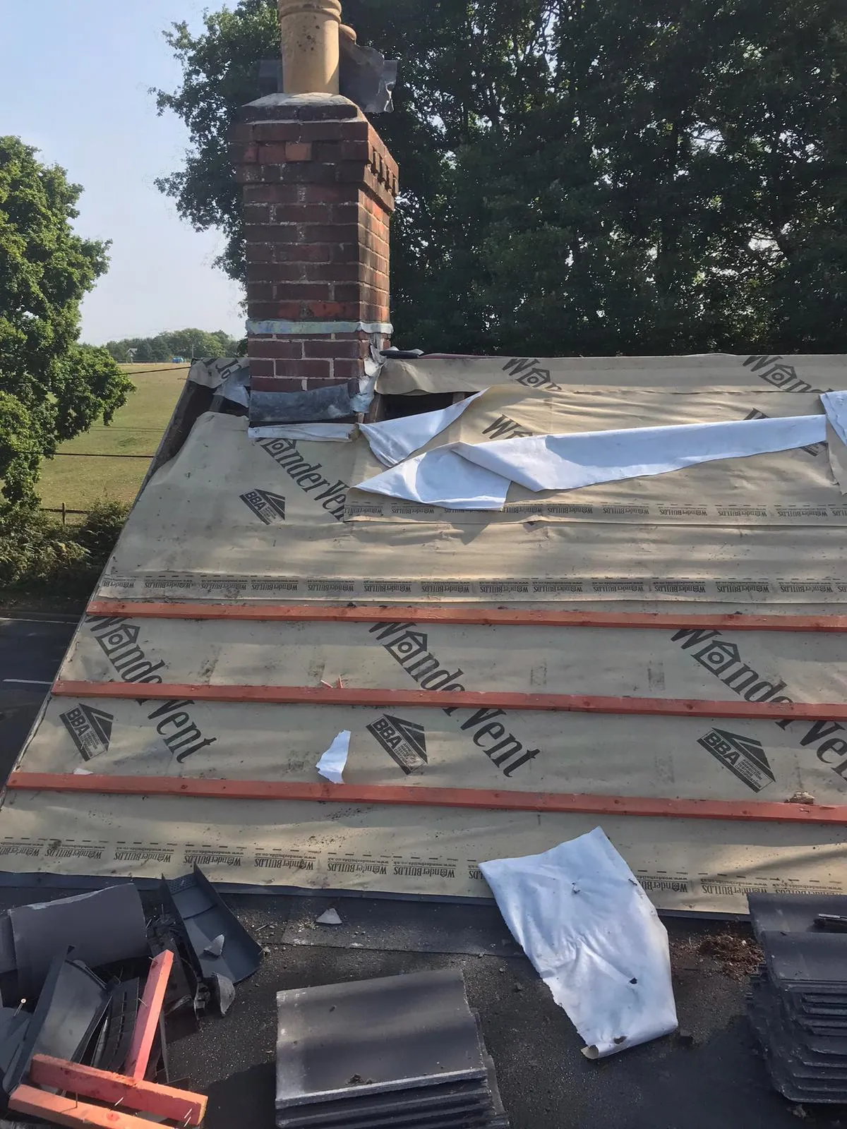 A pitched roof under construction, showing underlay, battens, and a brick chimney stack.