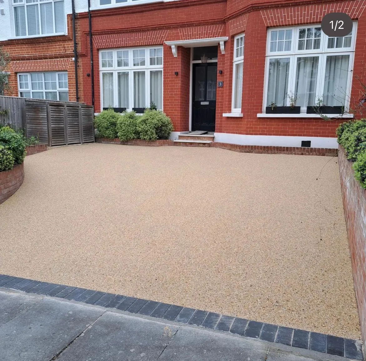 A modern resin-bound driveway completed by Top Pave Driveways LTD, featuring a light aggregate mix and a dark block paving edge, in front of a residential property.