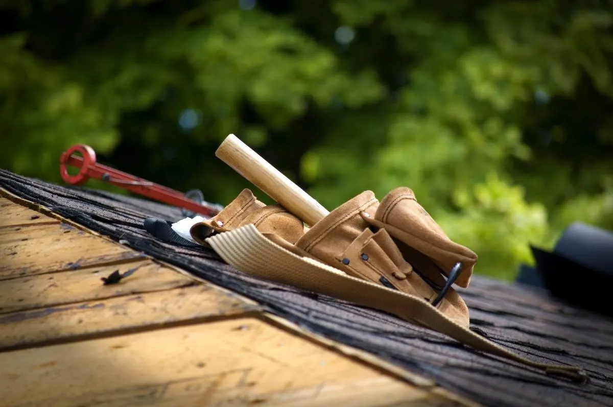 Roofing tools, including a hammer and tool belt, on a residential roof under construction or repair.