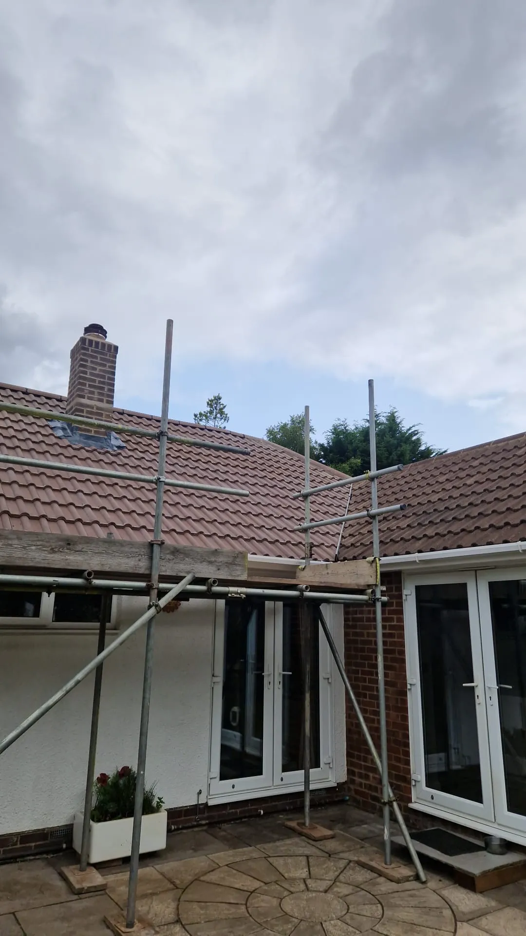 Scaffolding erected in front of a residential house with a brown tiled roof and brick chimney, ready for roofing work or repair.