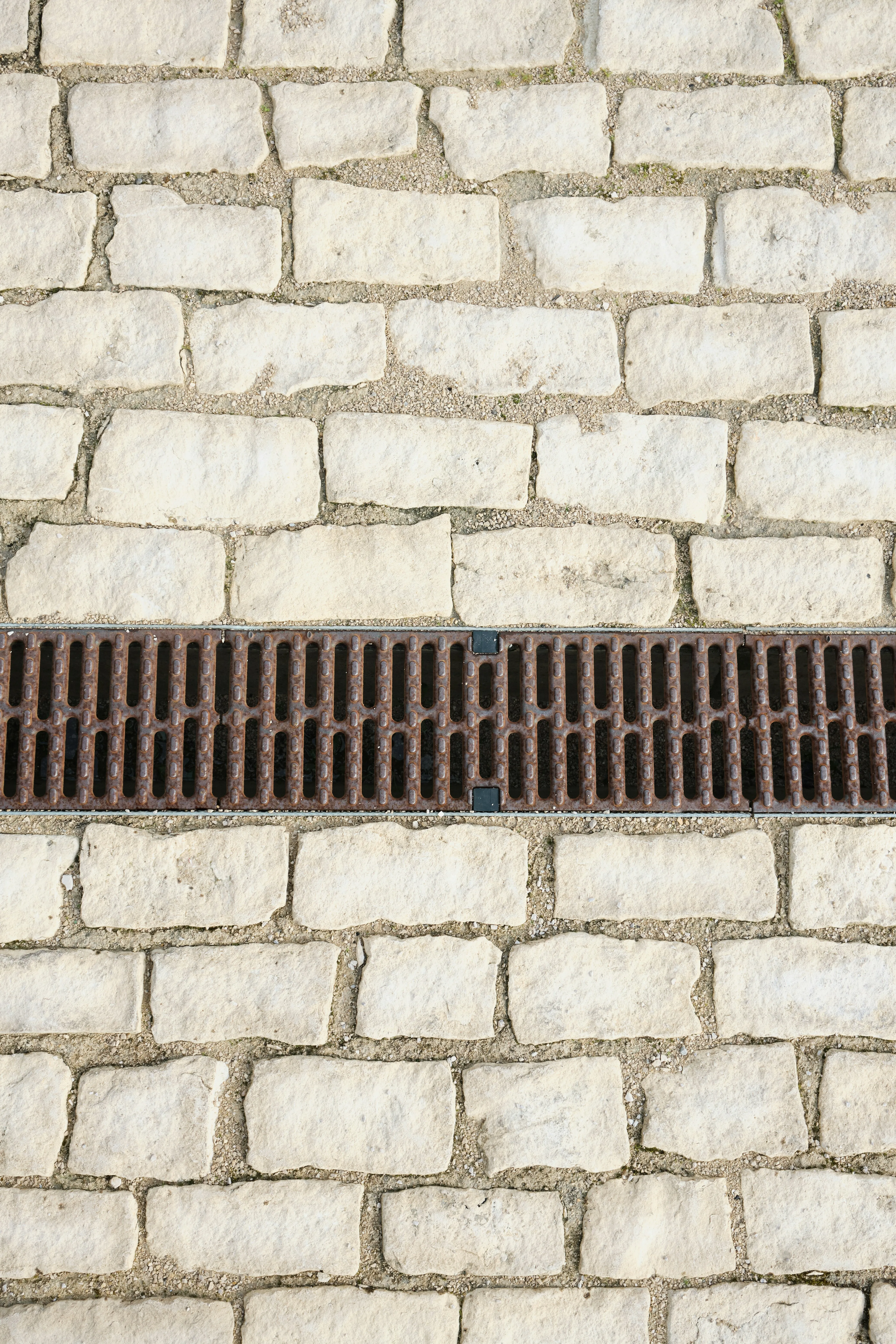 Light-coloured paving stones with a metal drain grate for drainage.