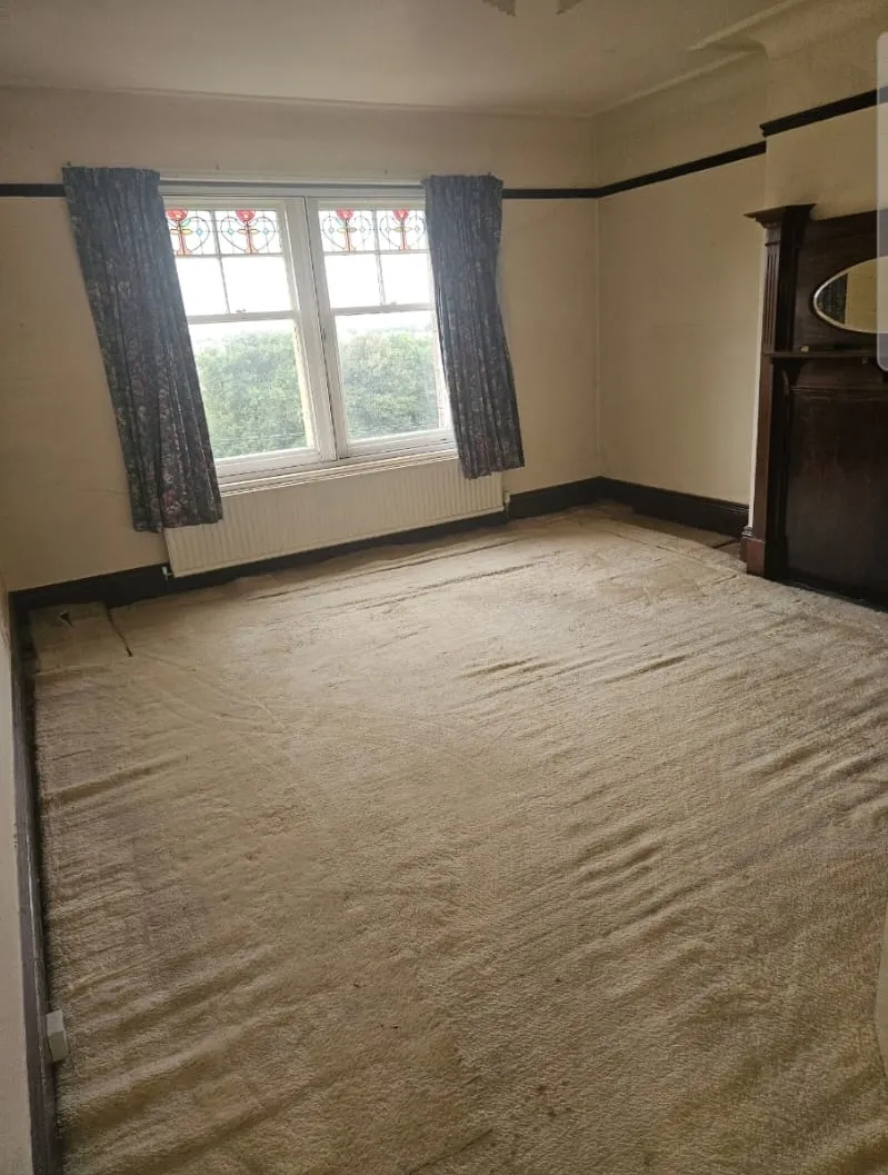An empty room with an old, dirty carpet and a window, typical of a property needing clearance.