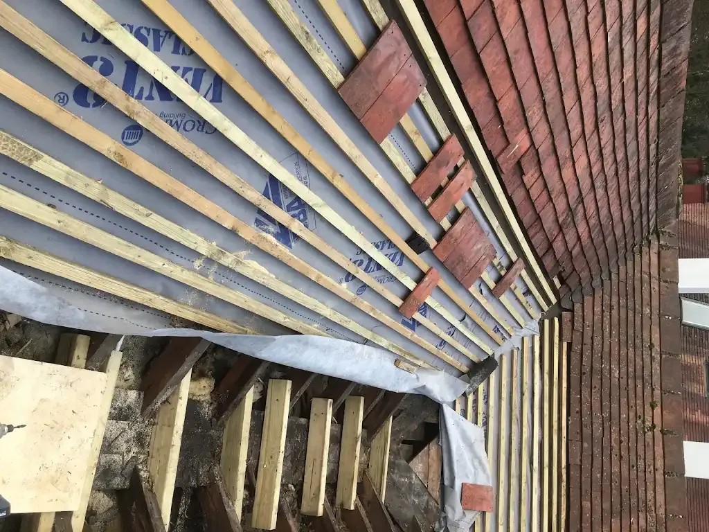Expert roof tiling process showing new battens, underlayment, and tiles being laid on a pitched roof.