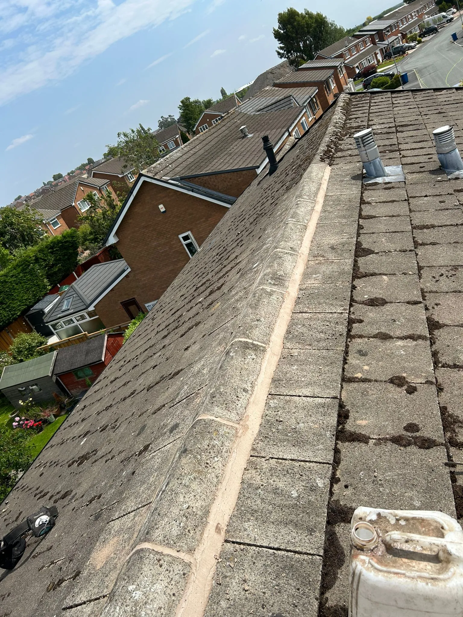 A tiled pitched roof with a newly repointed ridge and visible moss on older tiles, suggesting cleaning and repair work by M. Woodward Roofing.