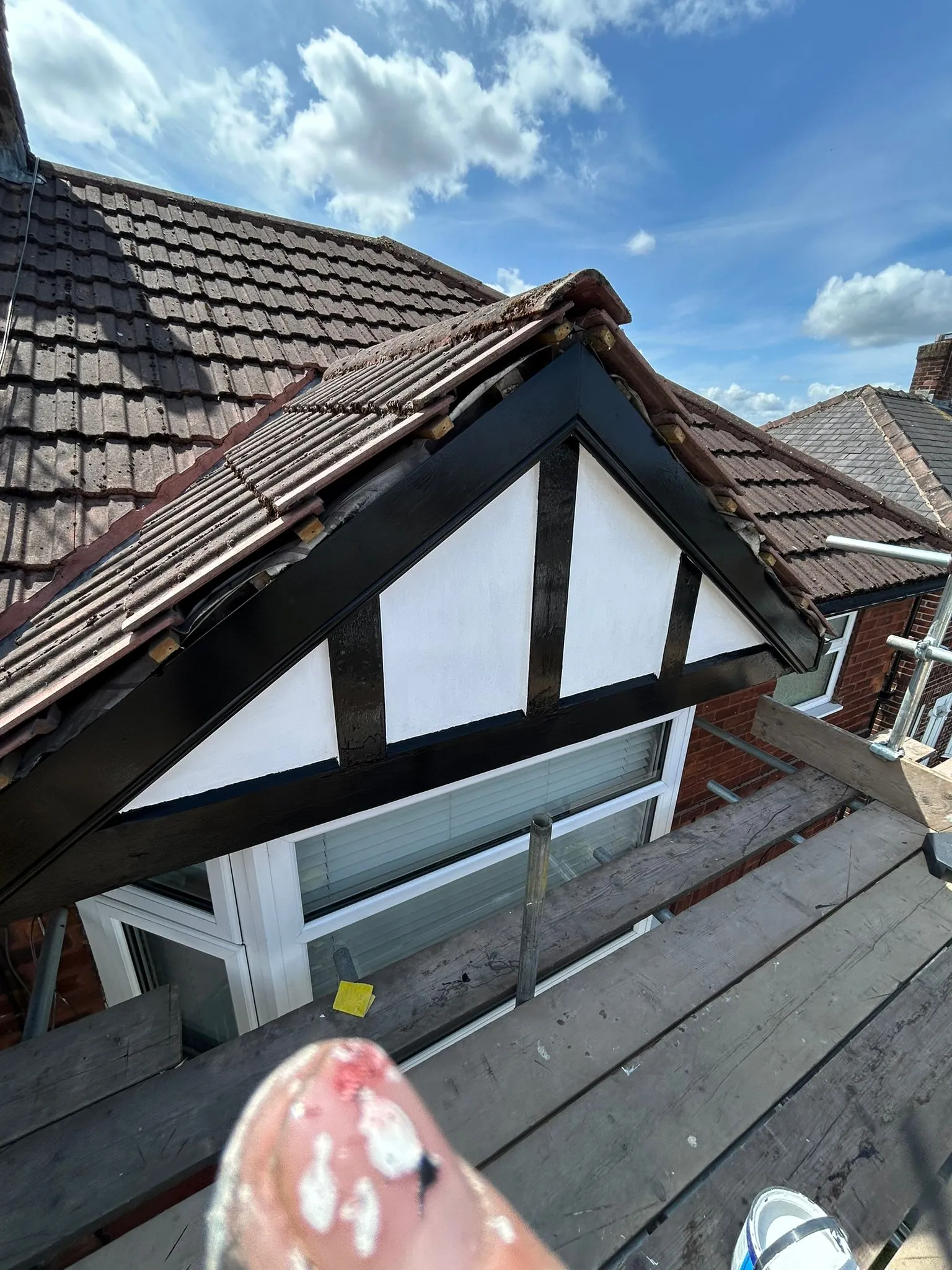 A close-up view of a house roof, showing a dormer window with newly painted black and white detailing, set against a brown tiled roof and blue sky.