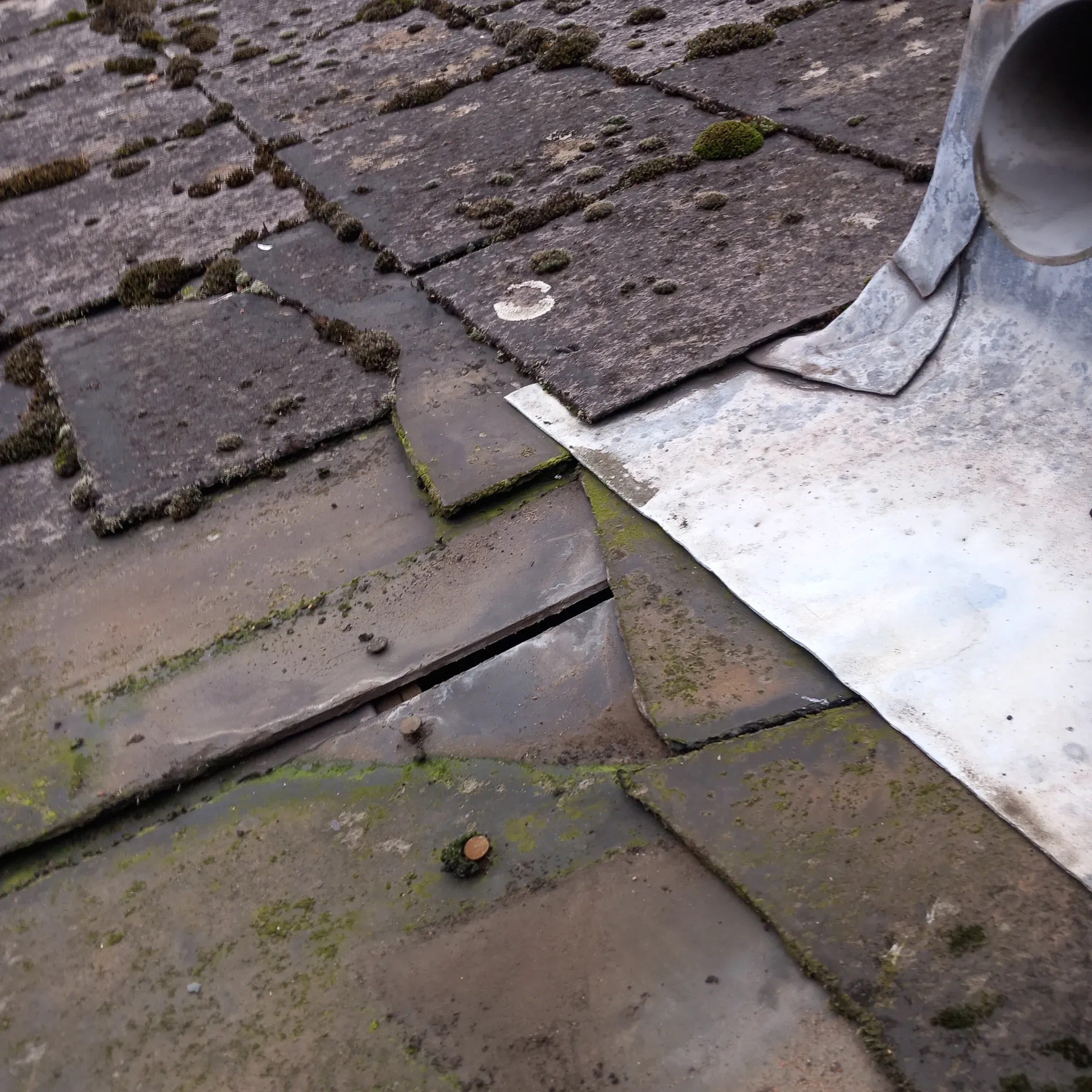 Close-up of a damaged, moss-covered tiled roof with a slipped tile and aged lead flashing, highlighting the need for roof repair in Leicester.