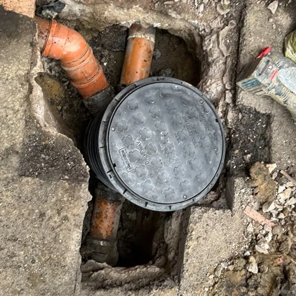 Drainage excavation showing new orange pipes and a manhole cover installed in a dug-up driveway