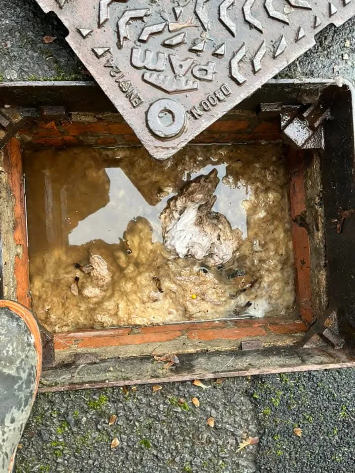 Blocked drain manhole overflowing with sewage and debris.