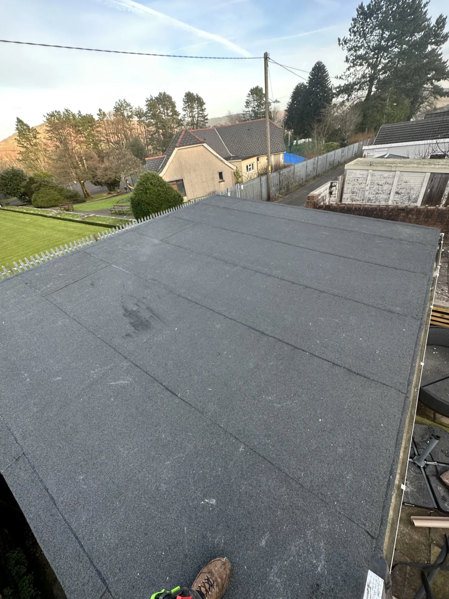 Newly installed dark grey flat roof with visible seams and bird spikes, overlooking a residential area.