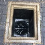 Open external drain gully showing dirty water and debris inside, suggesting a blockage or need for cleaning.