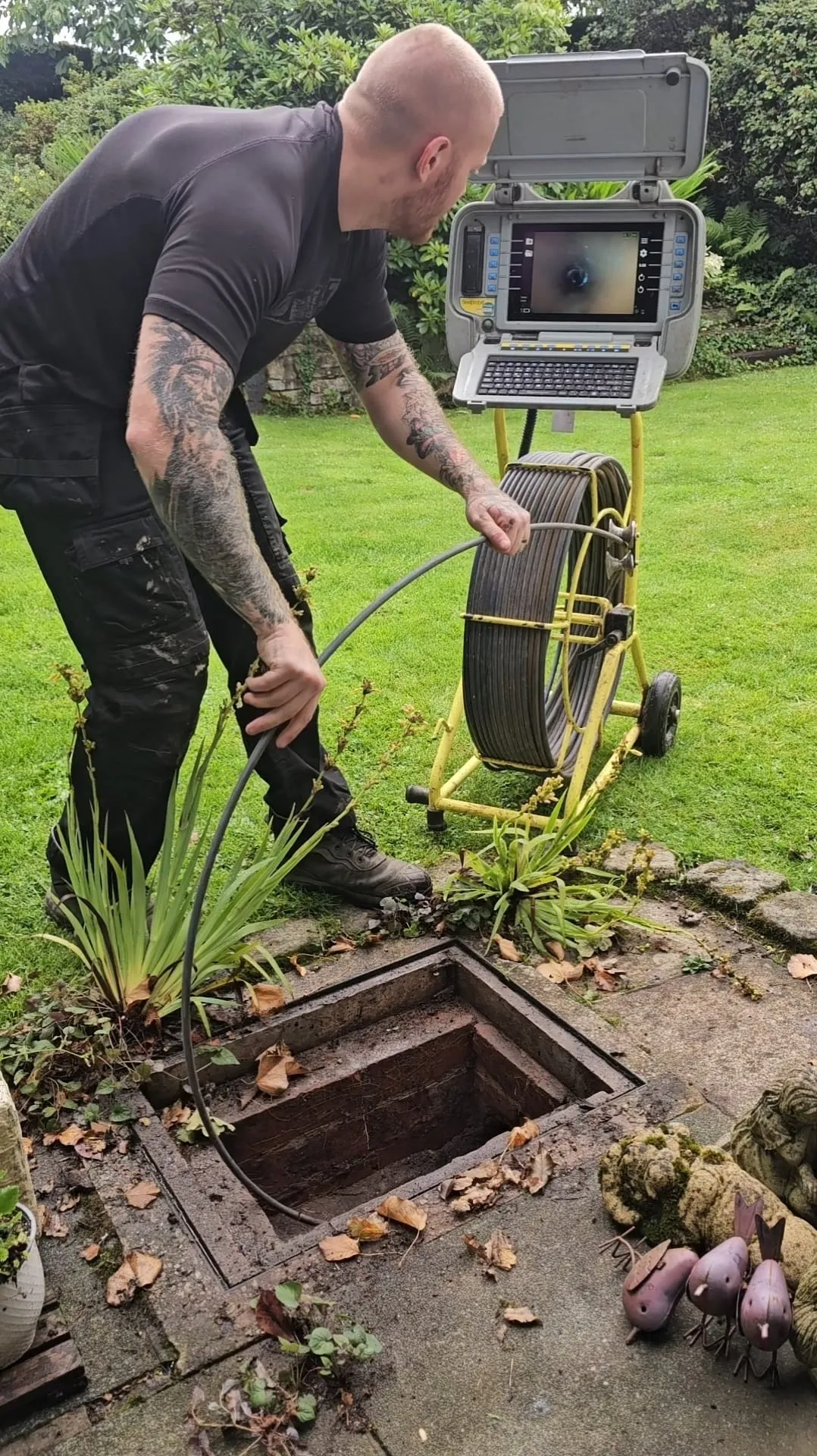 A picture of a drainage engineer operating a CCTV drain camera system near an open manhole.