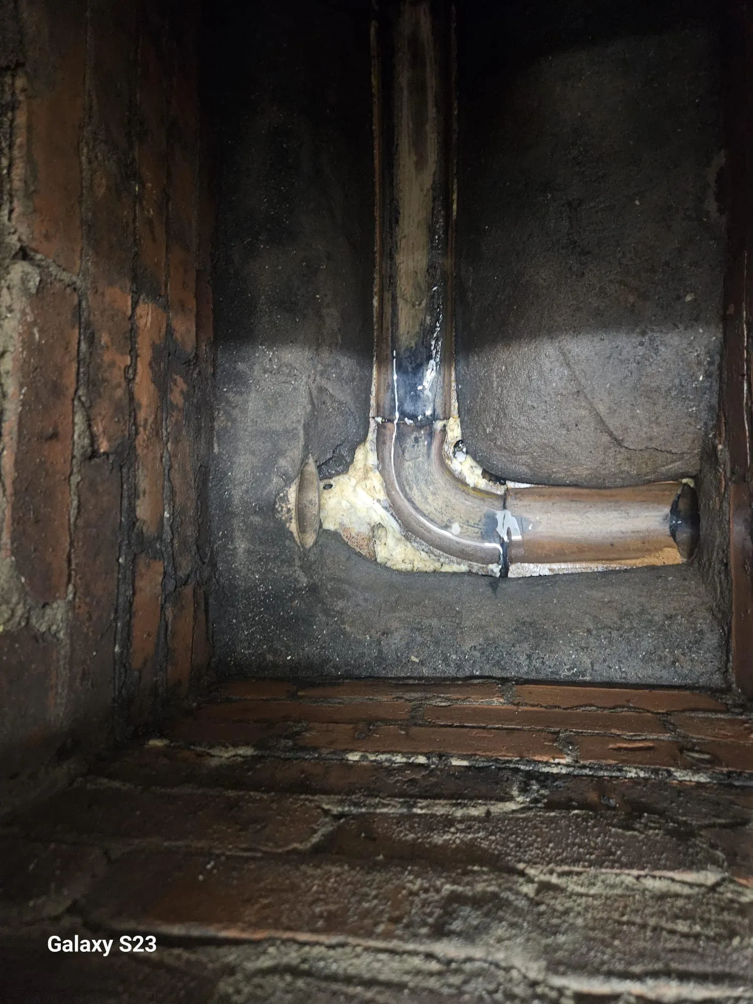 Close-up of old or existing drainage pipework and its connection point inside a brick wall.