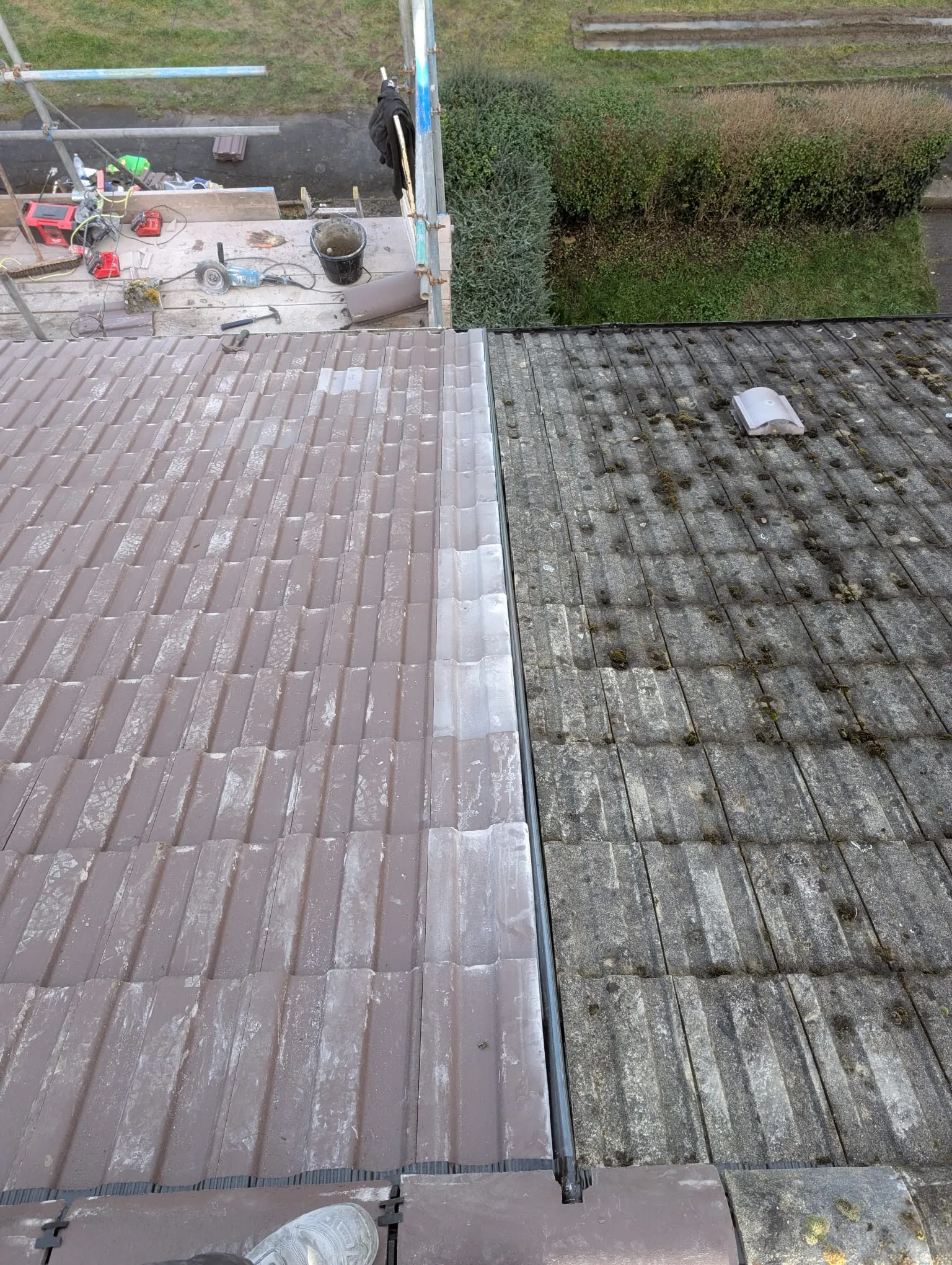 Before and after roof cleaning: one section of a tiled roof is clean and free of moss, while the adjacent section remains dirty with significant moss growth.
