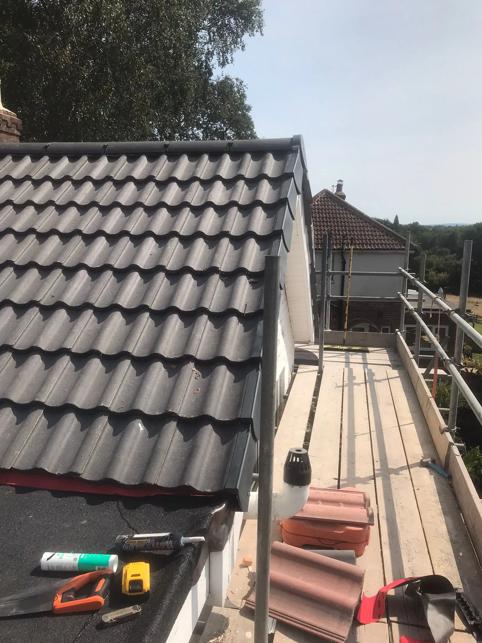 New grey tiled roof meeting a flat roof with roofing tools, scaffolding, and residential background.