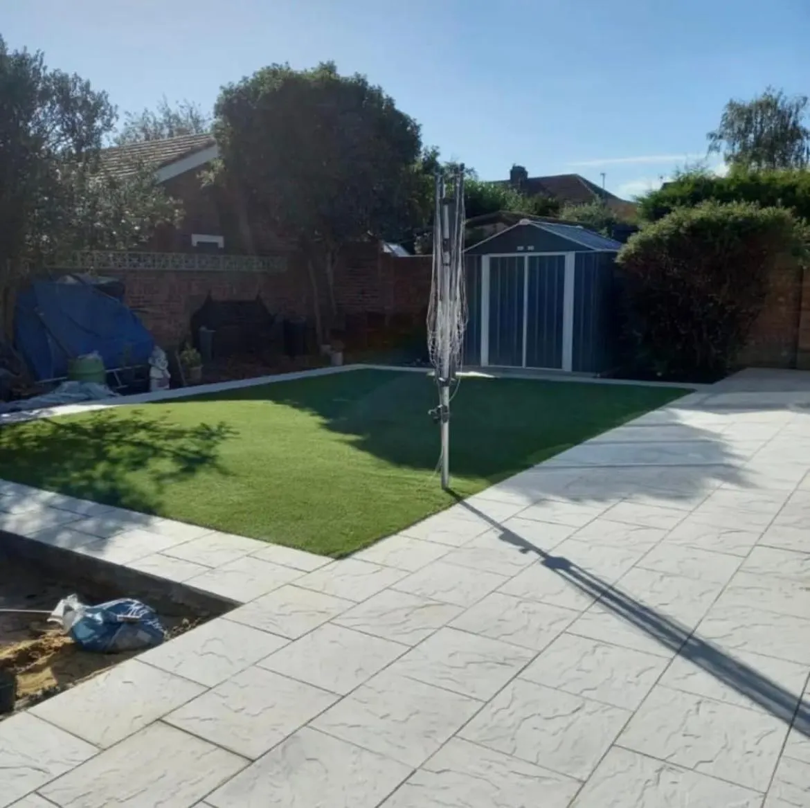 Modern backyard with new light grey patio paving and artificial grass installed.