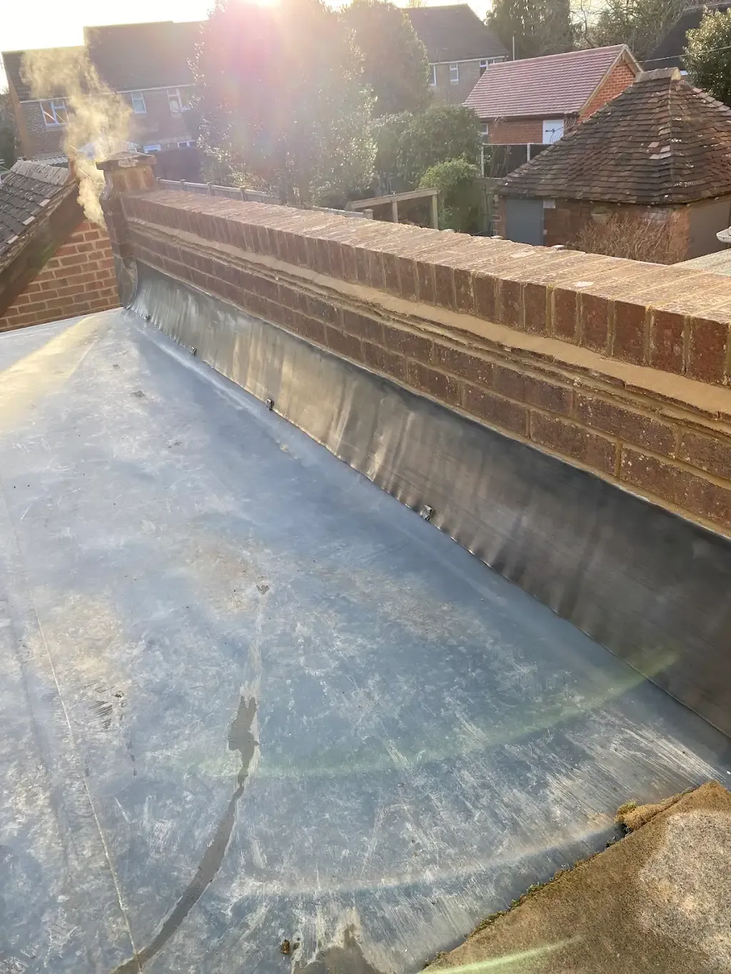 Lead flashing installed on a flat roof next to a brick chimney stack.