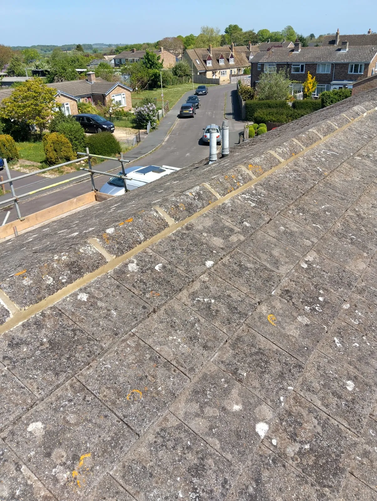 A residential roof with weathered concrete tiles and a fresh mortar line, overlooking a suburban street.