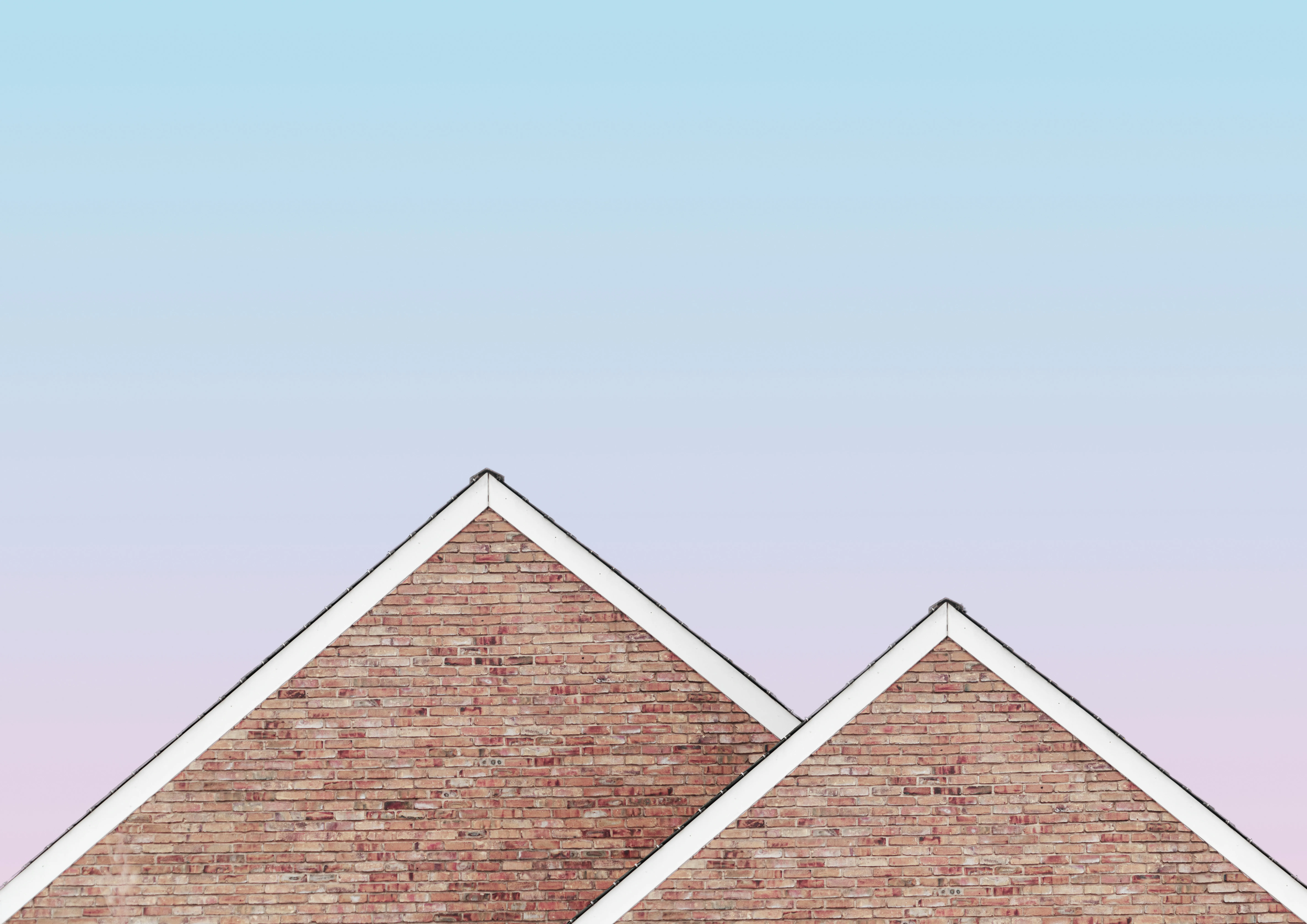 Modern brick gable ends of a building with crisp white roofline details and a clear sky background, highlighting clean construction and design.