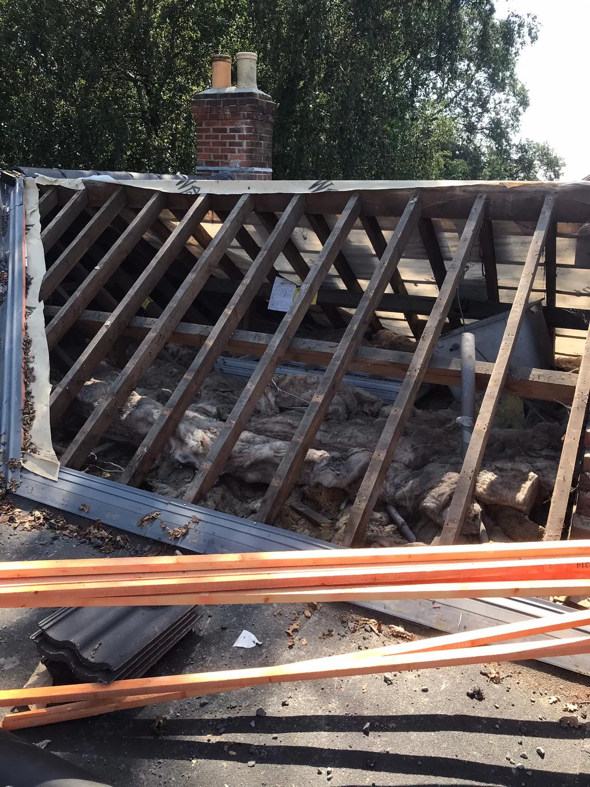 Pitched roof construction or renovation showing exposed wooden rafters, insulation, a chimney, and new roof tiles on site.
